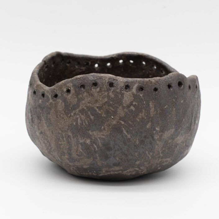 Cuenco de cerámica negro de estilo rústico con los bordes perforados.